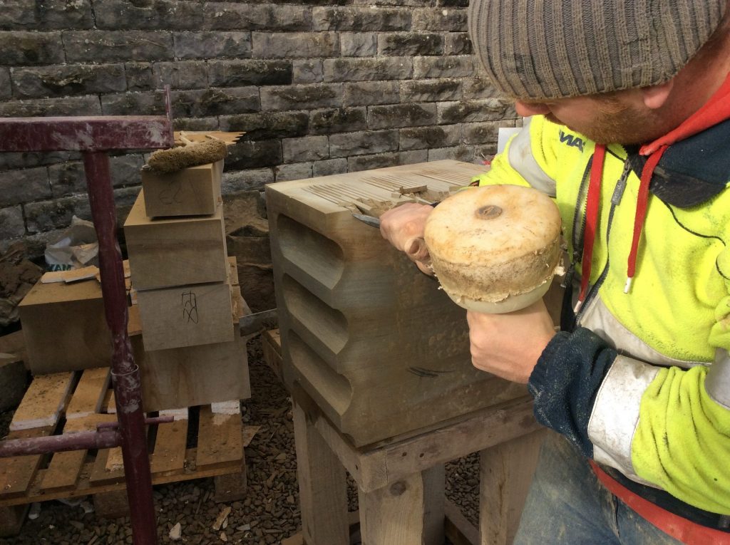 A stonemason carving a piece of stone on a historic building